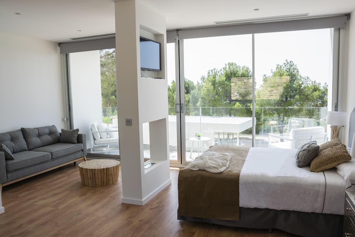 A modern bedroom with a large bed, a grey sofa, and a balcony with a table and chairs.