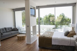 Un dormitorio moderno con una cama grande, un sofá gris y un balcón con mesa y sillas.