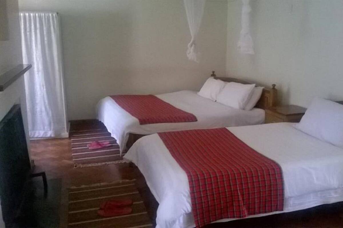 A hotel room with two beds, each with white linens and red blankets. There is a wooden floor and a small table with a chair.