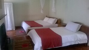 A hotel room with two beds, each with white linens and red blankets. There is a wooden floor and a small table with a chair.