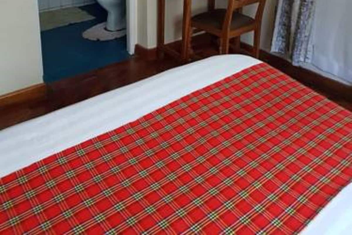 A hotel room with a bed, a wooden chair, a small table, a bathroom with a toilet, and a shower area.