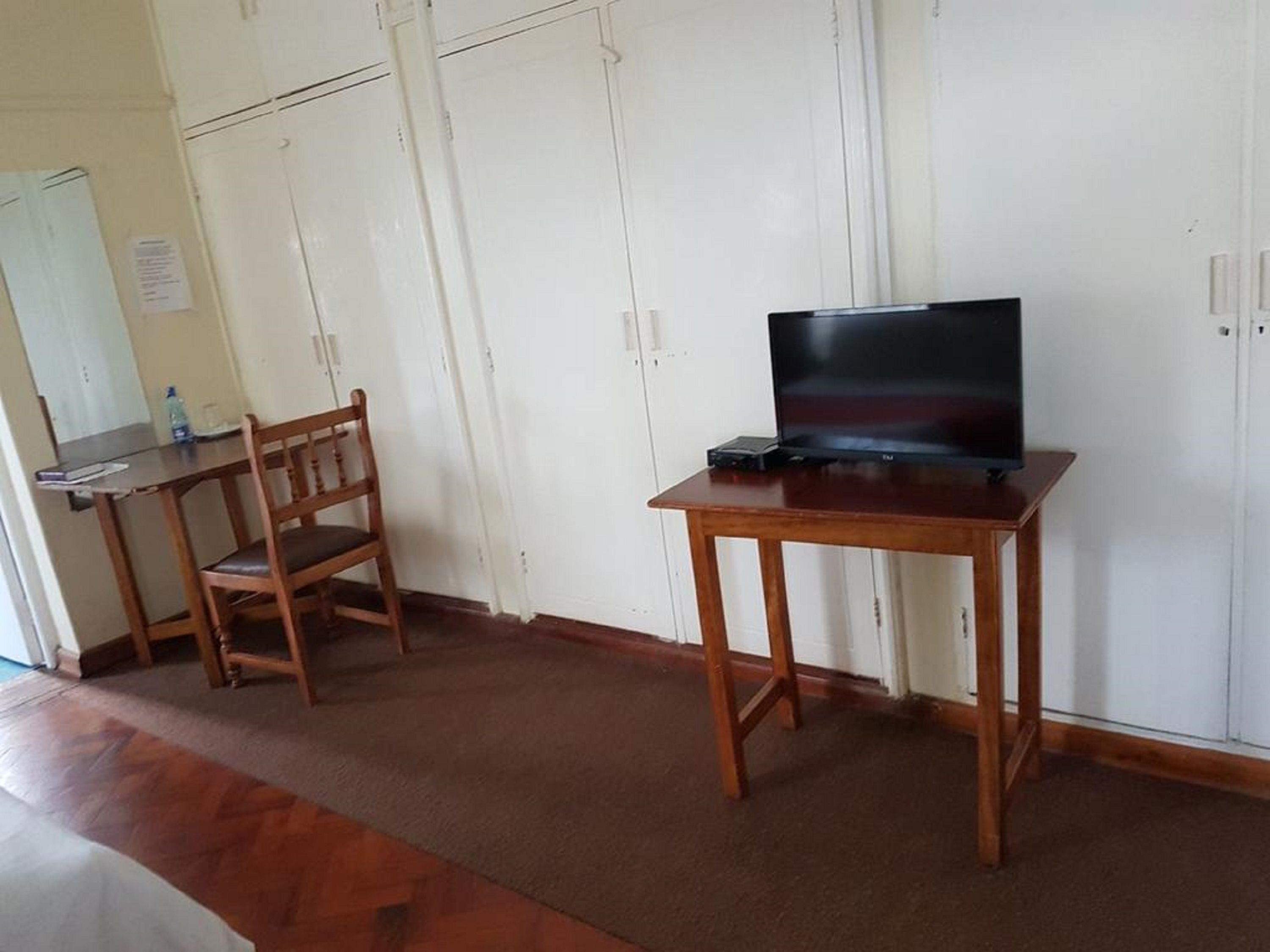 A room with a wooden desk, a chair, a television on a stand, and white cabinets.