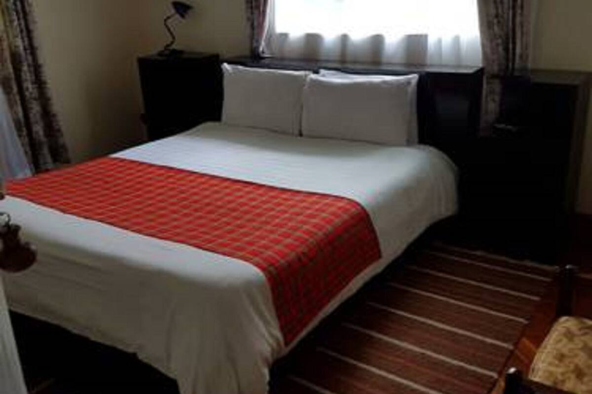 A neatly made bed with a red and white bedspread, a wooden floor, a chair, and a nightstand with a lamp.