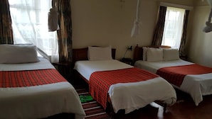 Een hotelkamer met drie bedden, elk voorzien van een rode geruite sprei en witte kussens. De kamer heeft een houten vloer en een raam met gordijnen.