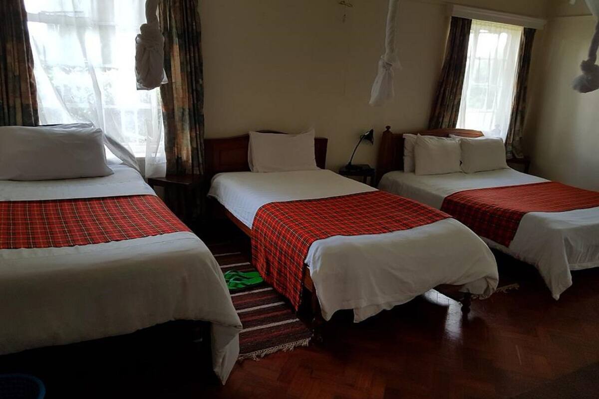 A hotel room with three beds, each with a red plaid bedspread and white pillows. The room has wooden flooring and a window with curtains.