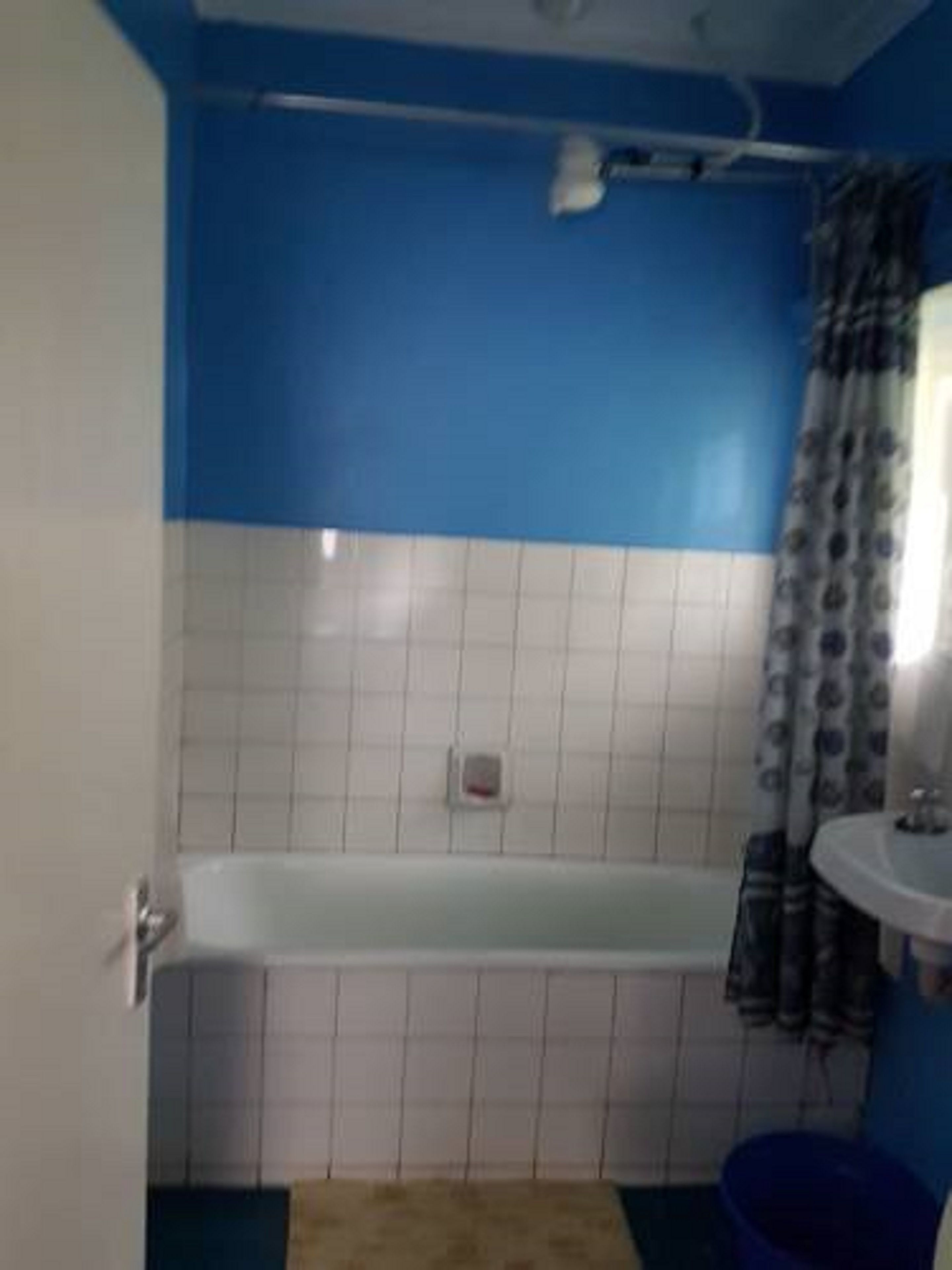 A bathroom with a bathtub, a shower curtain, a sink, and a blue bucket.