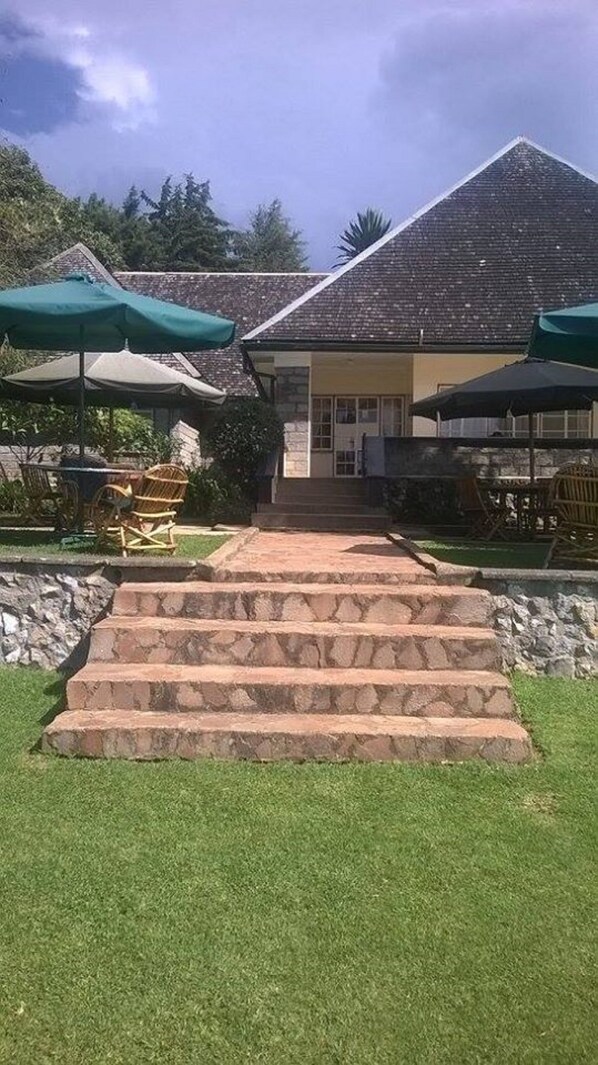 A building with a stone staircase leading to a door, surrounded by grass and outdoor furniture.