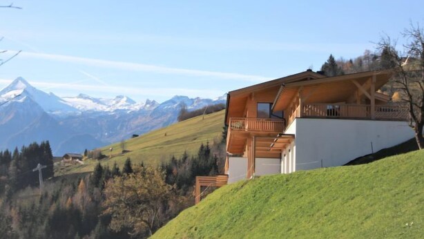Un chalet doté d’un balcon, situé dans un cadre magnifique, avec des montagnes enneigées en toile de fond et un ciel dégagé.