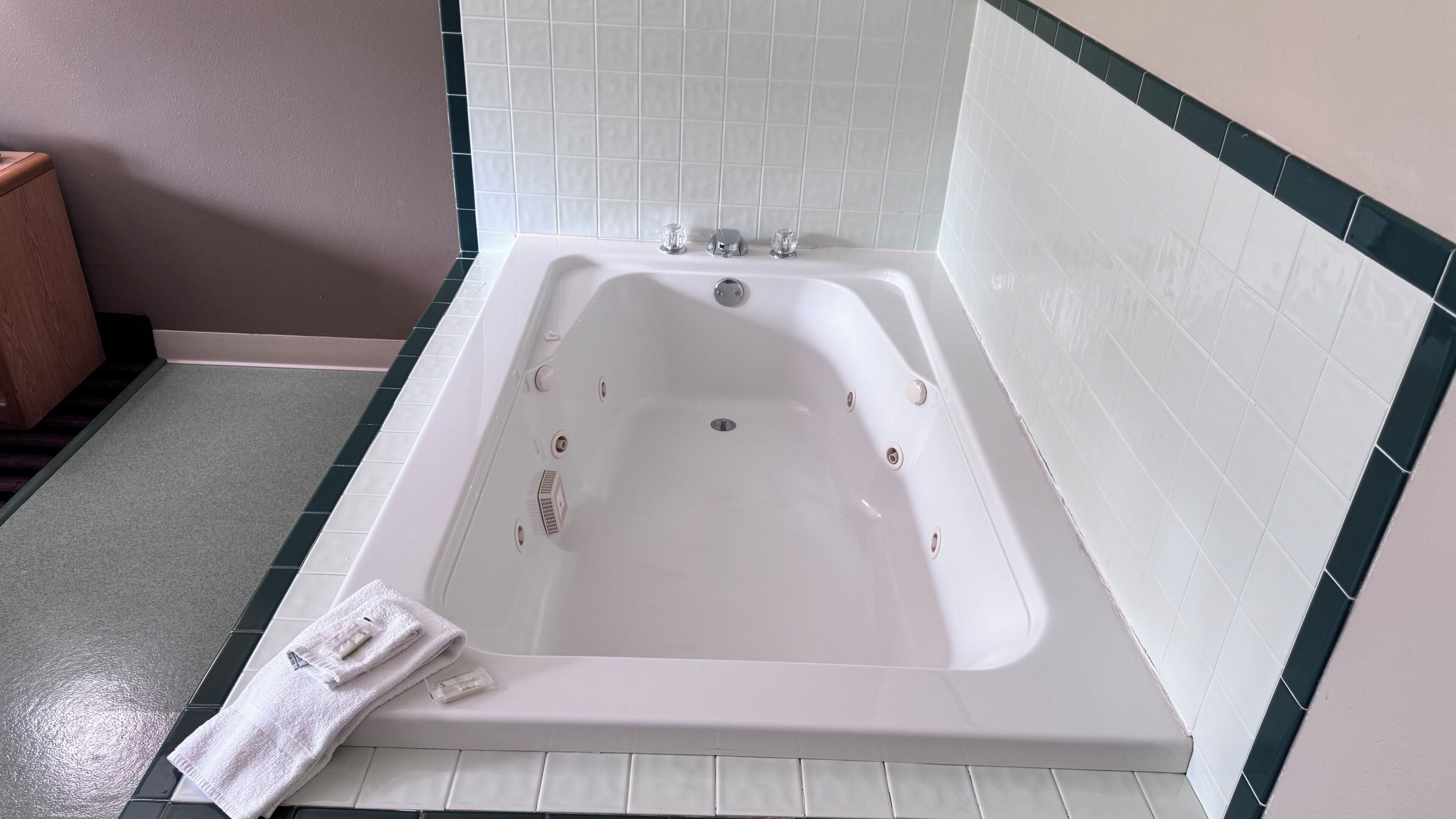 A white bathtub with a showerhead, a towel, and a green and white tiled wall.