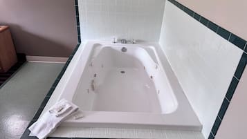 A white bathtub with a showerhead, a towel, and a green and white tiled wall.