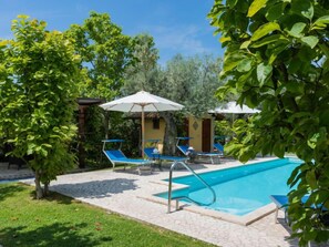 Une piscine entourée de verdure et d’un sentier en pierre, avec des chaises longues et des parasols à proximité.