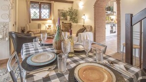 A dining area with a checkered tablecloth, set for a meal. There is a sofa in the background, a kitchen visible through an archway, and a decorative vase on the table. - Olive Grove Sabina by Interhome (Castelnuovo di Farfa)