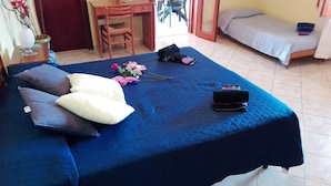 Una habitación con una cama, un escritorio y una silla. Hay almohadas en la cama y un jarrón con flores.