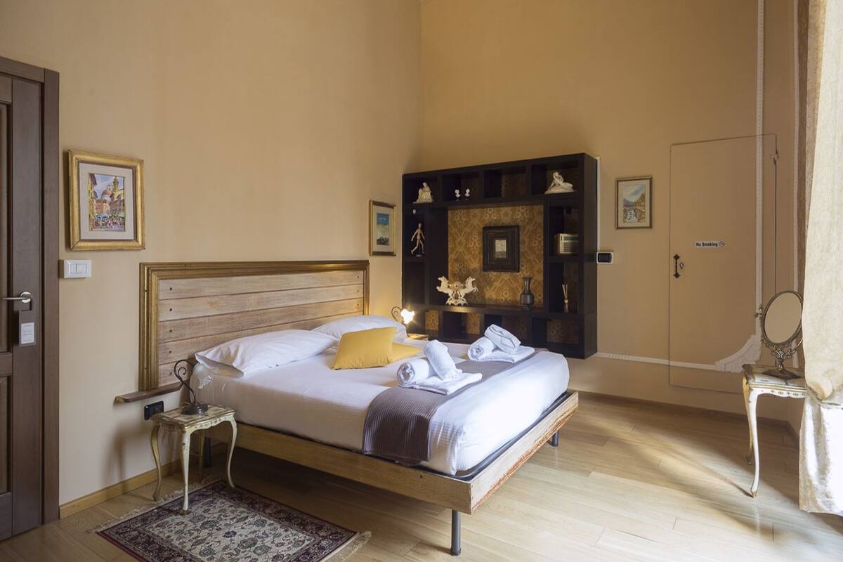 A bedroom with a wooden bed, a nightstand, a bedside table, a mirror, a wardrobe, and a small rug.