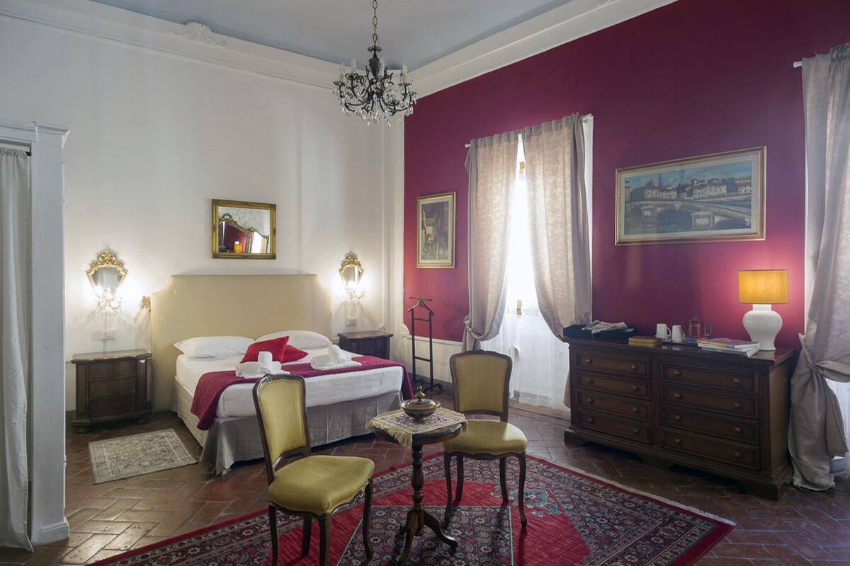 A room with a bed, two chairs, a table, a dresser, and a chandelier.