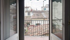 Blick von einem Balkon mit Metallgeländer auf eine Straße mit Häusern mit Terrakotta-Dachziegeln und einem Schornstein.