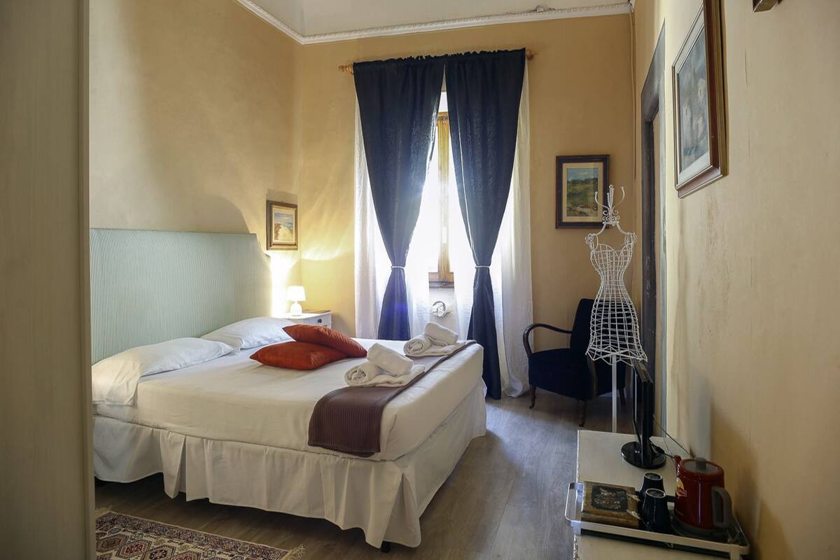 A hotel room with a bed, a chair, a desk with a lamp, and a window with curtains.