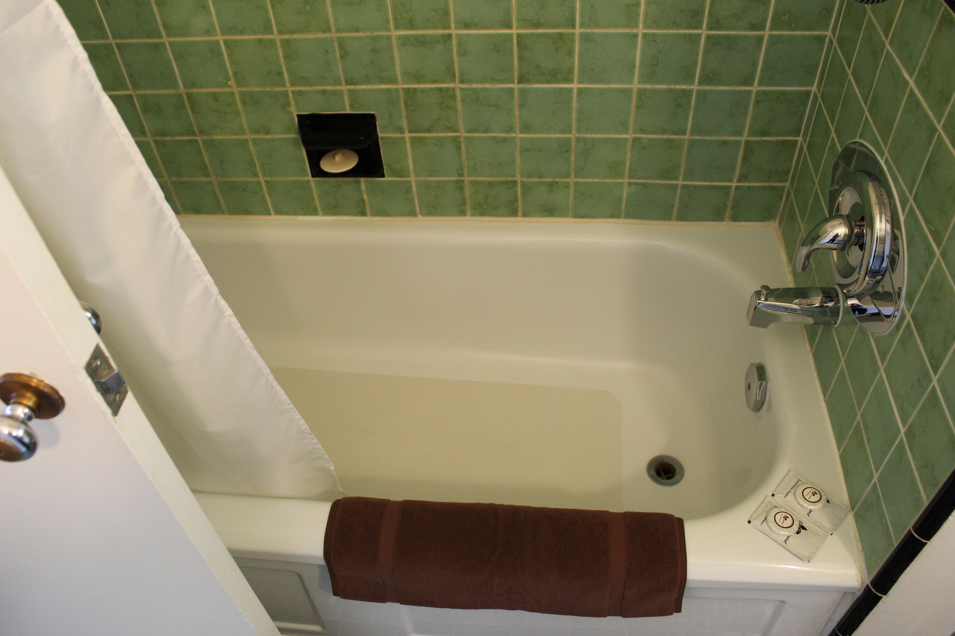 A bathroom with a bathtub, green tiled walls, a white door, and a brown towel hanging on the wall.
