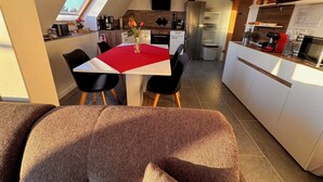 A modern kitchen with white cabinets, a red tablecloth, and a dining area with black chairs. - 85 m² apartment, 3 rooms, kitchen, shower, 15 m² south-west facing balcony (Leipzig)