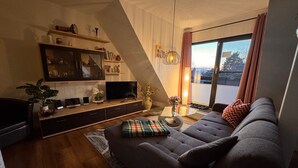 A living room with a sofa, TV, and shelves with decorative items. - 85 m² apartment, 3 rooms, kitchen, shower, 15 m² south-west facing balcony (Leipzig)