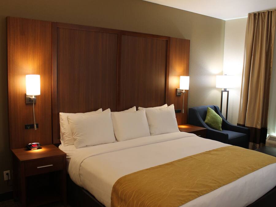 A hotel room with a large bed, two bedside lamps, a nightstand, a chair, and a window with curtains.