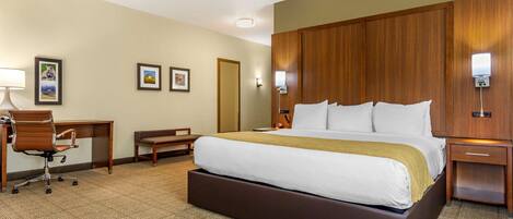 A hotel room with a large bed, a desk, a chair, and a small table.