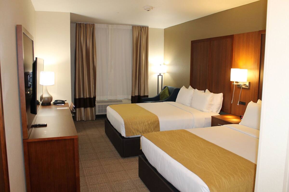 Une chambre d’hôtel avec deux lits, un bureau, une télévision, une lampe et une fenêtre avec des rideaux.