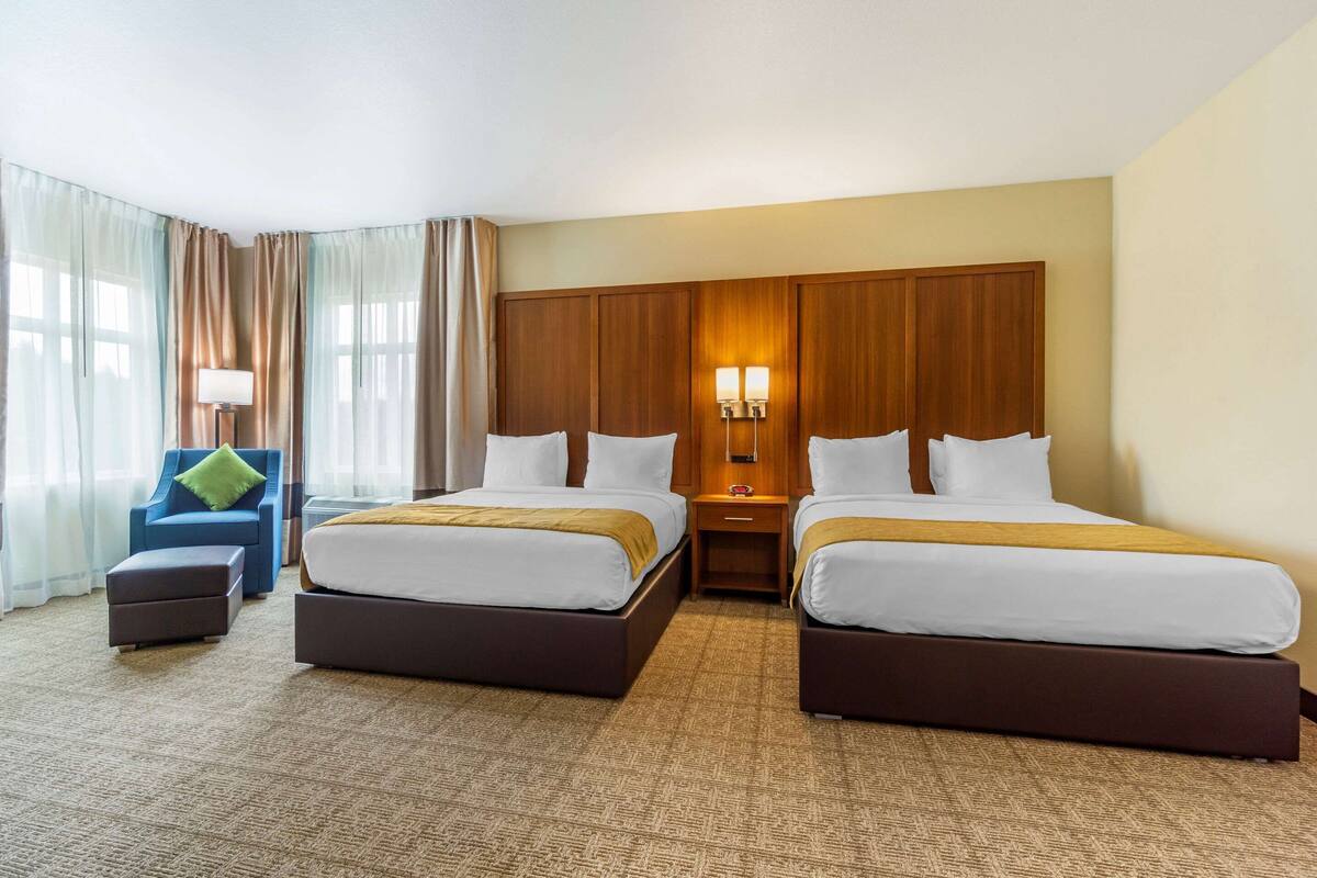 Une chambre d’hôtel avec deux lits, un bureau, une chaise et une grande fenêtre avec des rideaux.