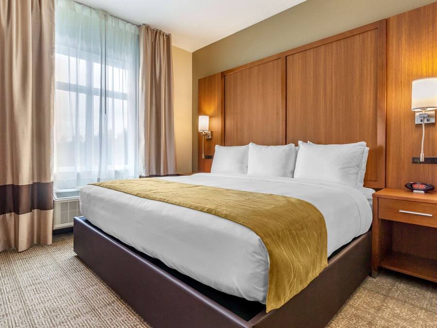 Een hotelkamer met een groot bed, een houten hoofdbord, bedlampen en een nachtkastje met een klok.