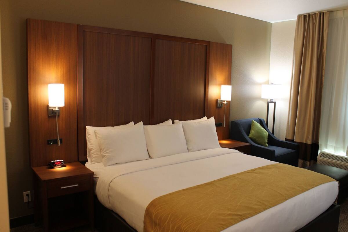 Une chambre d’hôtel avec un grand lit, deux tables de chevet, un bureau, une chaise et une fenêtre avec des rideaux.