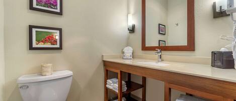 A bathroom with a toilet, sink, mirror, and shelves with towels.