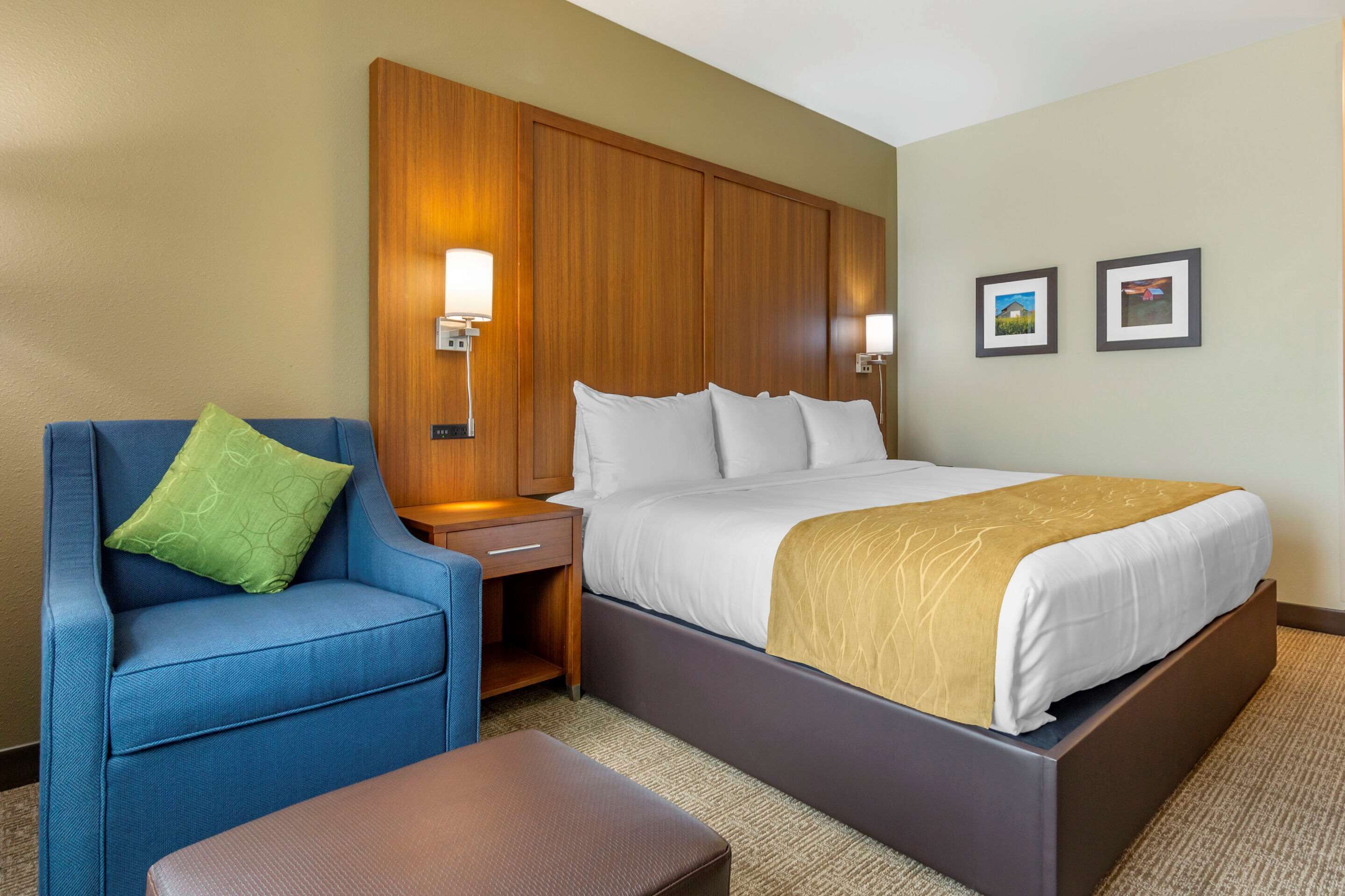 A hotel room with a bed, a blue armchair, a wooden nightstand, and two wall-mounted lamps.