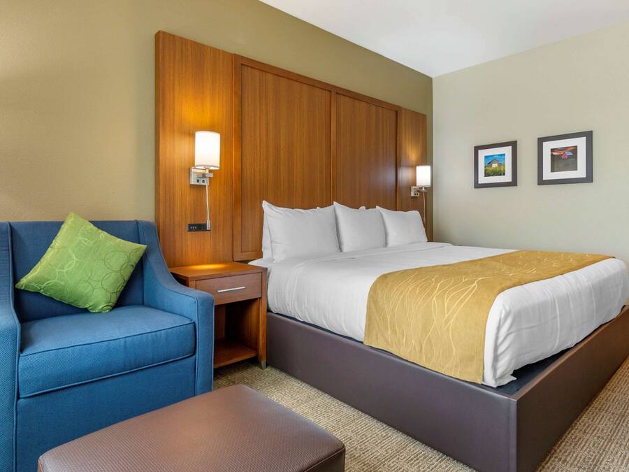 A hotel room with a bed, a blue armchair, a wooden nightstand, and two wall-mounted lamps.