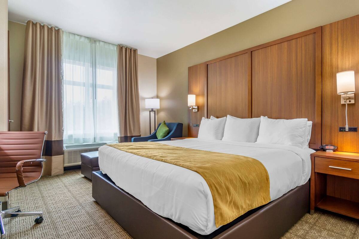 Une chambre d’hôtel avec un grand lit, un bureau, une chaise et une fenêtre avec des rideaux.
