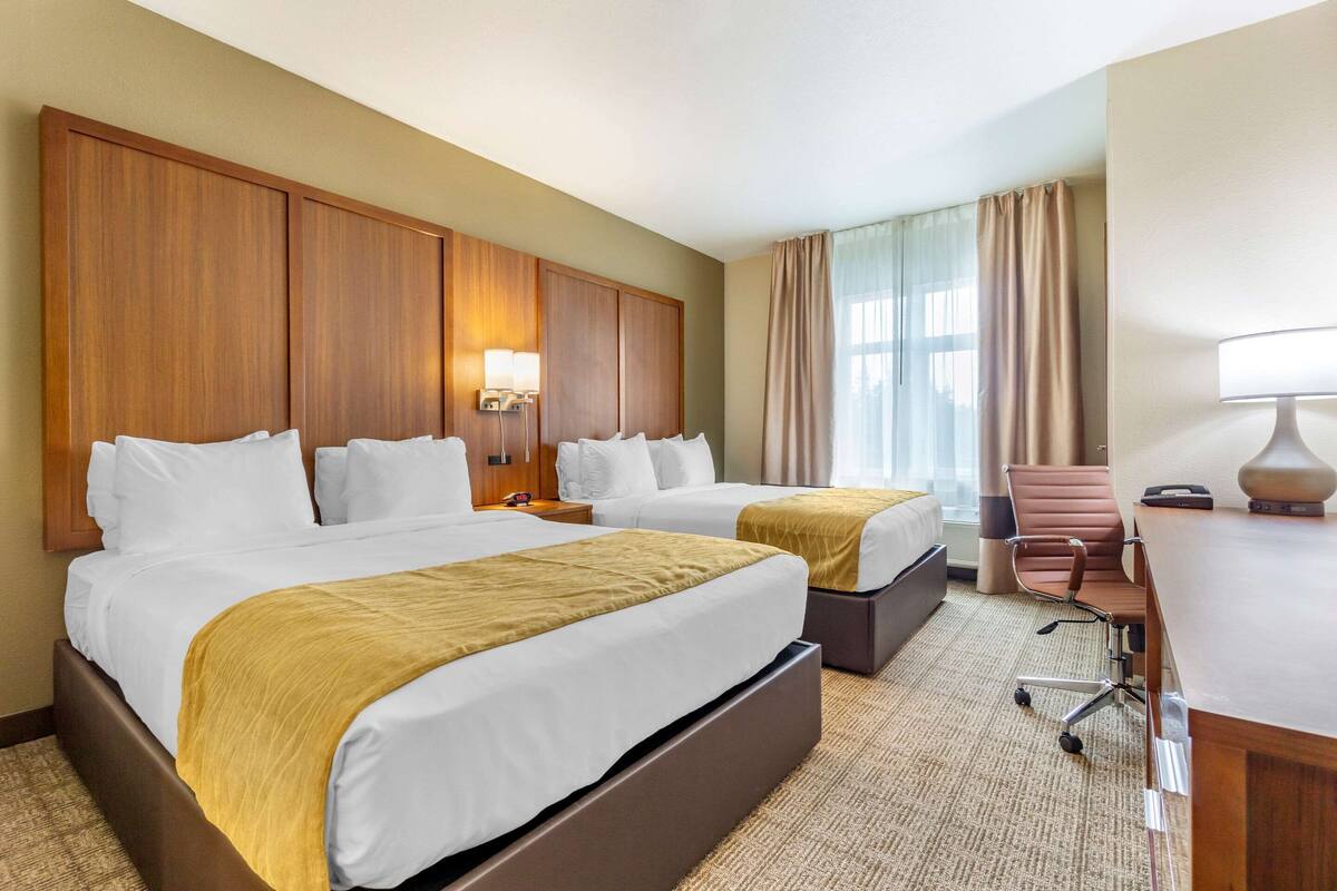 Une chambre d’hôtel avec deux lits, un bureau, une chaise et une grande fenêtre avec des rideaux.