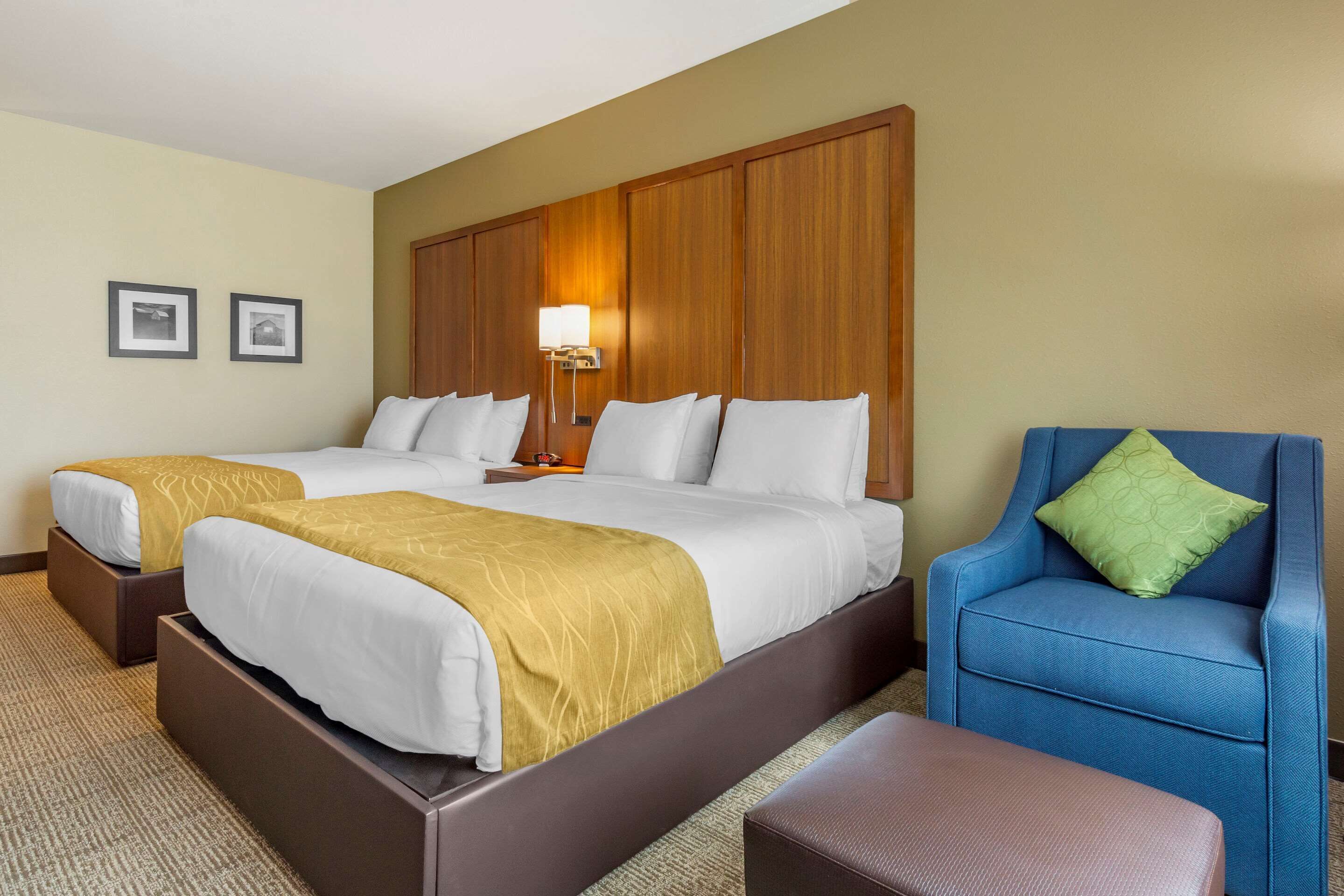 Habitación de hotel con dos camas, un sillón azul y un cabecero de madera.