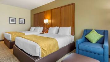 Habitación de hotel con dos camas, un sillón azul y un cabecero de madera.