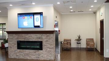 A lobby with a stone fireplace, a flat-screen TV displaying the Google and Apple logos, two wooden chairs, and a potted plant.
