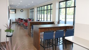 A spacious indoor area with a long wooden table and blue chairs, large windows, and a clock on the wall. - Comfort Inn & Suites Lakewood by JBLM (Lakewood)