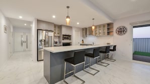 A modern kitchen with a central island, bar stools, stainless steel appliances, and pendant lighting. - 34 Madaffari Drive - Pet friendly Marina Property (Exmouth)