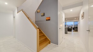 A modern interior with a wooden staircase, a grey wall with artwork, and a view to a living area. - 34 Madaffari Drive - Pet friendly Marina Property (Exmouth)