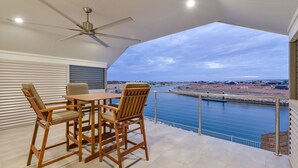 A balcony with a table and chairs, a ceiling fan, and a view of a body of water and distant buildings. - 34 Madaffari Drive - Pet friendly Marina Property (Exmouth)