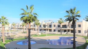 A modern hotel with multiple-story buildings, a central pool area, and palm trees.