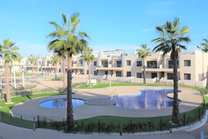 Un hôtel moderne composé de plusieurs bâtiments à étages, doté d’un espace piscine central et agrémenté de palmiers.
