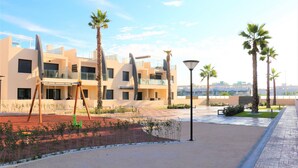A modern building with multiple floors, outdoor seating, and palm trees.