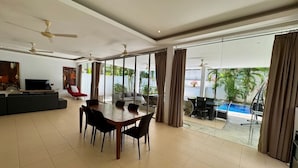 Un vaste espace de vie comprenant une salle à manger avec table et chaises, ainsi qu’un téléviseur. Une piscine est visible à travers de grandes fenêtres.