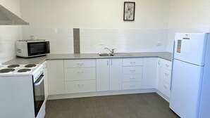 Eine kleine Küche mit weißen Schränken, einem Herd, einer Mikrowelle, einem Spülbecken und einem Kühlschrank.