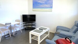 Ein kompakter Wohnraum mit Fernseher, einem kleinen Tisch, einer Couch und einem Bild mit Strandmotiv.