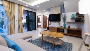 A modern living room with a sofa, coffee table, TV, and a kitchen area with a TV and shelves. - Rooftop Villa - Brand New 3BR Villa (Tambon Rawai)