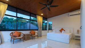 A modern bedroom with a large bed, two wicker chairs, a small table, and a ceiling fan. - Rooftop Villa - Brand New 3BR Villa (Tambon Rawai)